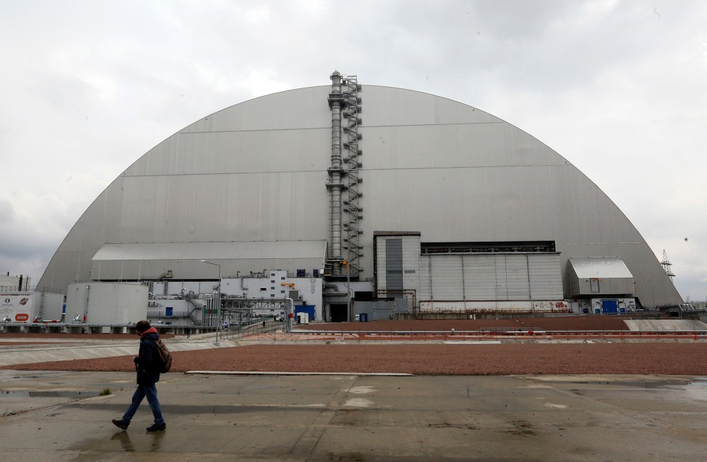 ARQUIVO - Um homem passa por um abrigo que cobre o reator explosivo na usina nuclear de Chernobyl, em Chernobyl, Ucrânia, quinta-feira, 15 de abril de 2021