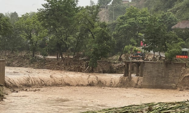 Um carro está ao lado de uma seção de uma ponte que foi levada pelas águas da inundação em Qingyang, noroeste da China