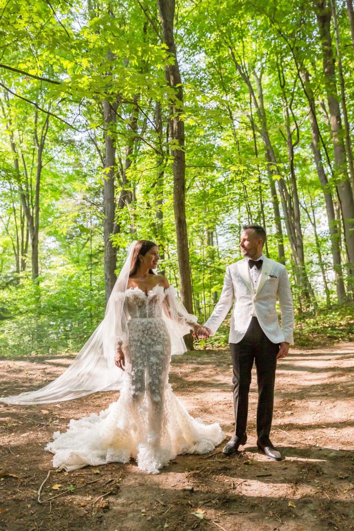 A noiva e o noivo se olham e dão as mãos em roupas de casamento na floresta.