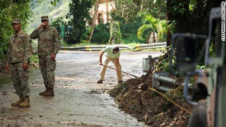 A Guarda Nacional orienta o trânsito em Caye, Porto Rico, onde o morador Luis Nogueira ajuda a limpar a estrada.