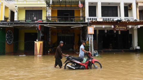 Pessoas empurram uma motocicleta em uma rua inundada na cidade de Hoi An, província de Quang Nam, em 28 de setembro de 2022.
